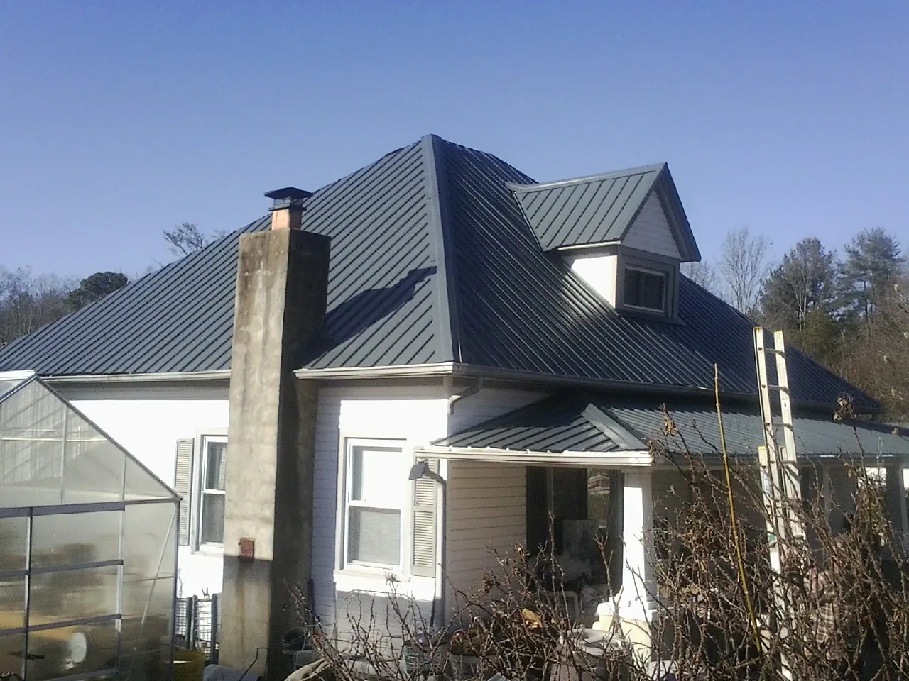 Dark blue standing seam metal roof on a white farmhouse with dormer — Slate & Tile Roof Repair by Roofing Brothers in Mount Solon