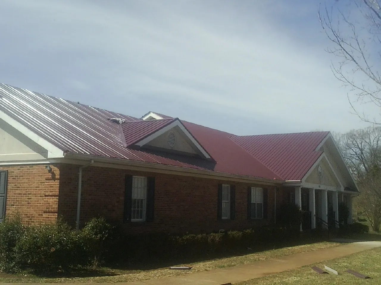 Red metal roof with gabled entries on a long brick building, from a Hail Damage Roof Repair job in Mount Solon