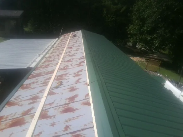 Old rusted panels beside newly installed green metal roofing — Wind Damage Roof Repair by Roofing Brothers in Mount Solon