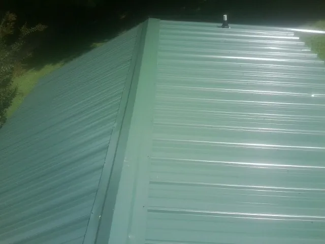 New green metal panels meeting at the ridge of a roof — Flat Roof Repair work by our crew in Mount Solon