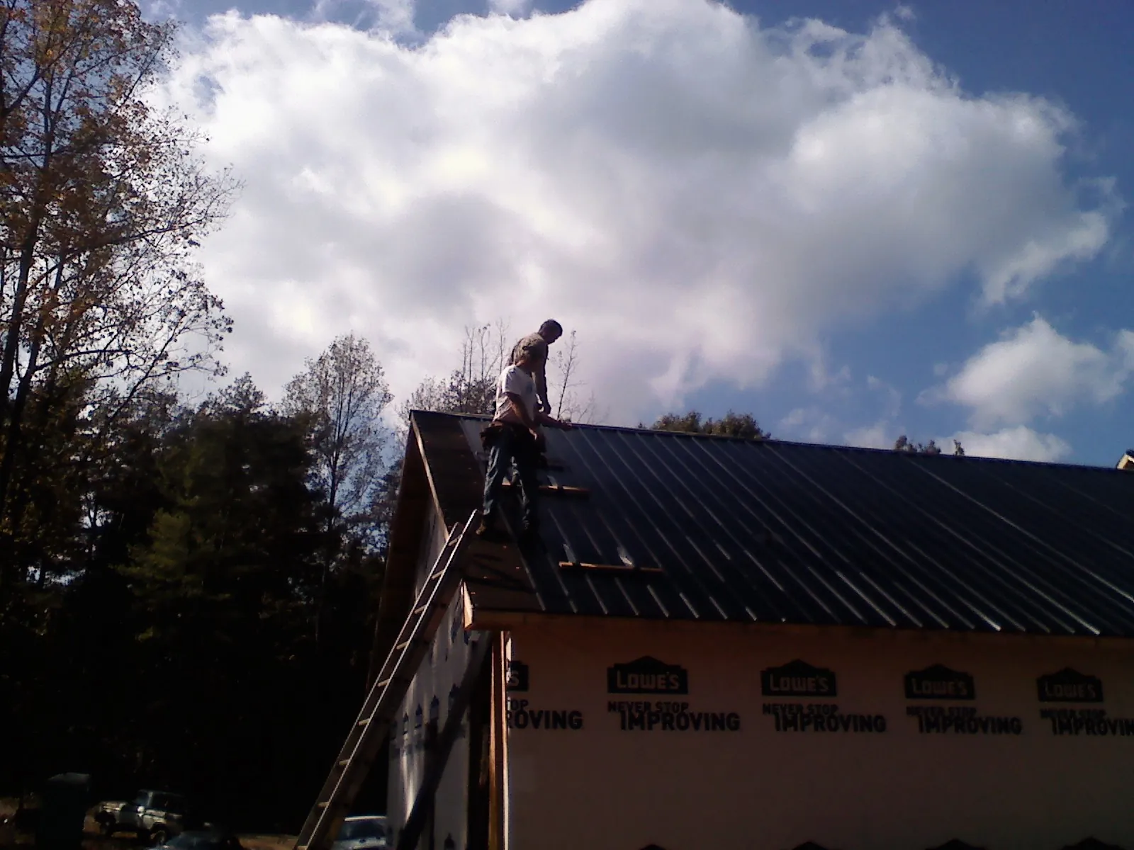 Roofer fastening dark metal panels high against a cloudy sky, from a Roof Inspection job in Mount Solon